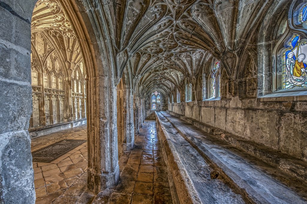 A long stone trough runs beneath windows and fan vaults, beside arched openings into the cloister walk.
