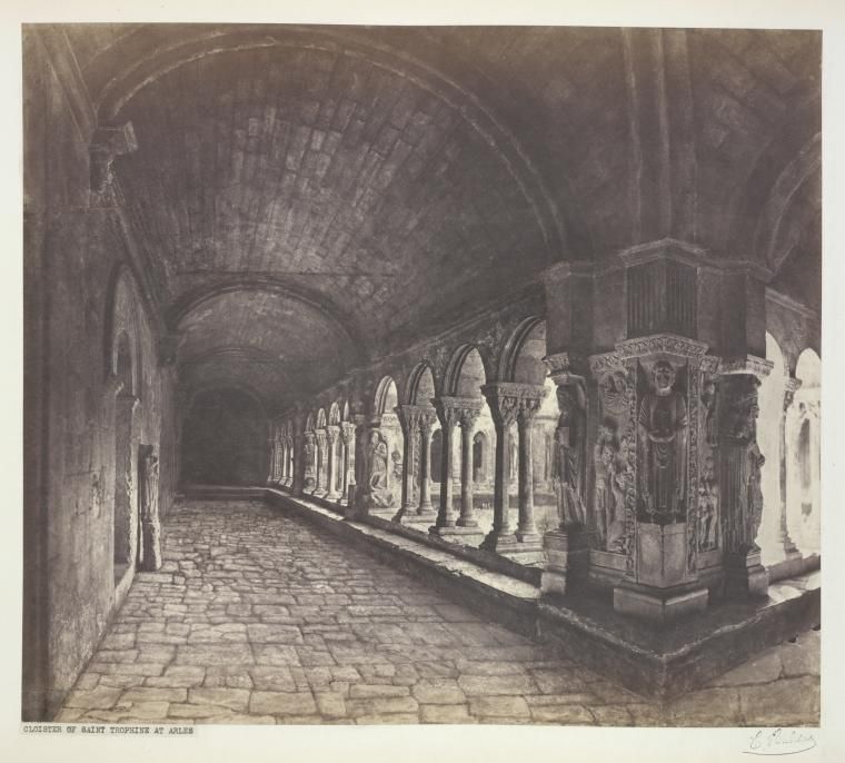 A historic monochrome photograph shows a paved barrel-vaulted walk, paired columns and a carved pier beside the open arcade.