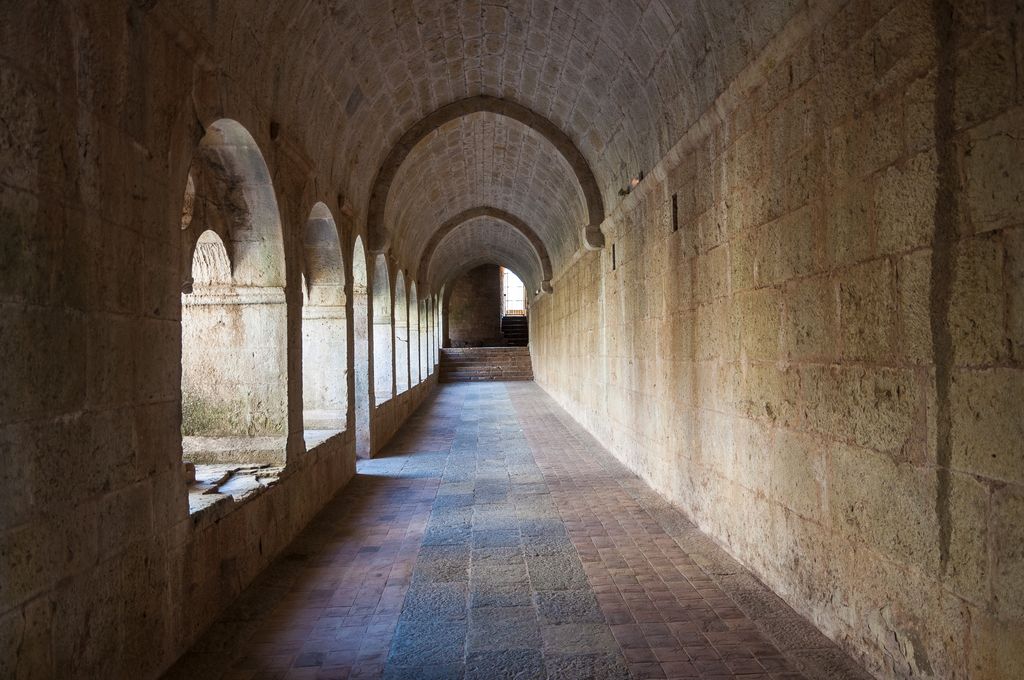 A stone gallery recedes beneath a barrel vault and transverse arches, with an open arcade to the left and steps ahead.