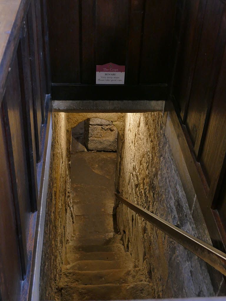 Worn stone steps descend between close masonry walls, with a handrail and a low opening at the bottom.