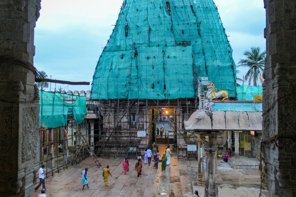 Green screening covers a gateway tower above scaffolding while visitors move through the entrance and across the stone court.