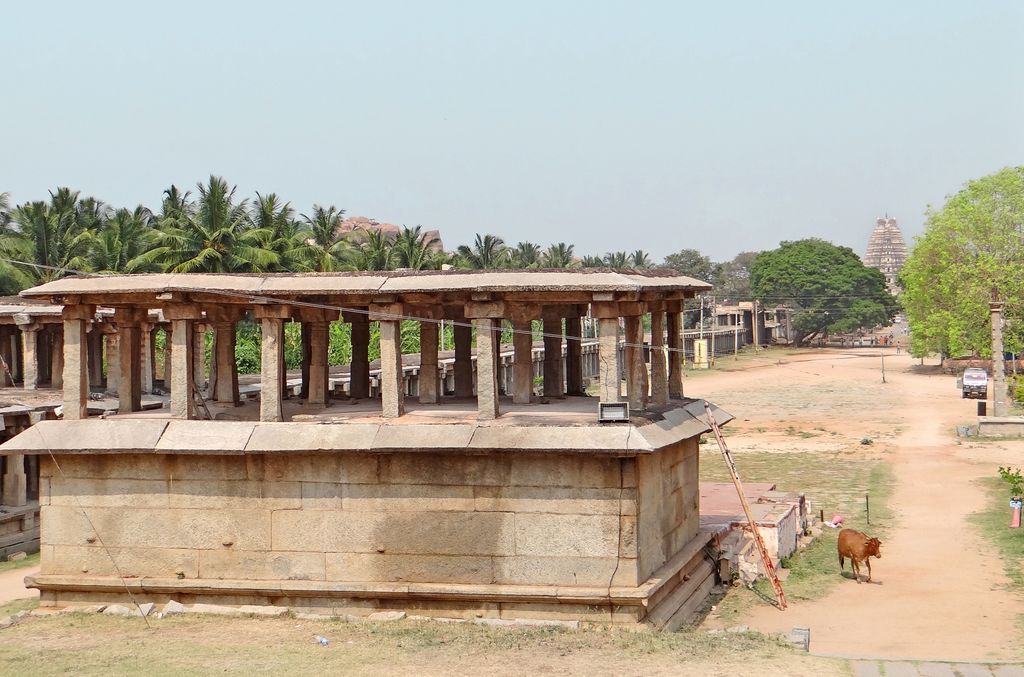 A raised stone pavilion with repeated columns borders a broad street leading to a distant temple gateway.