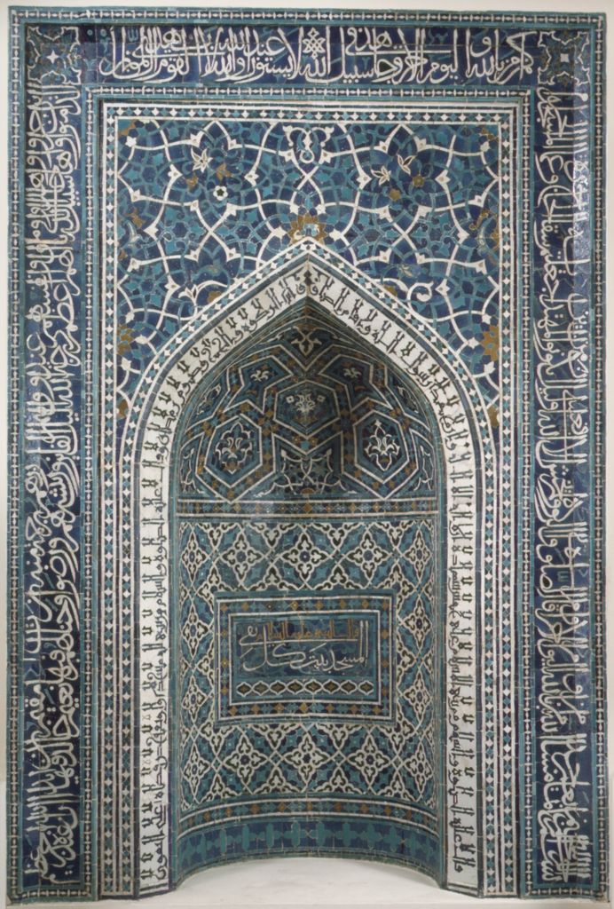 Blue, turquoise and white mosaic tiles form a rectangular inscribed frame around a deep pointed prayer niche.