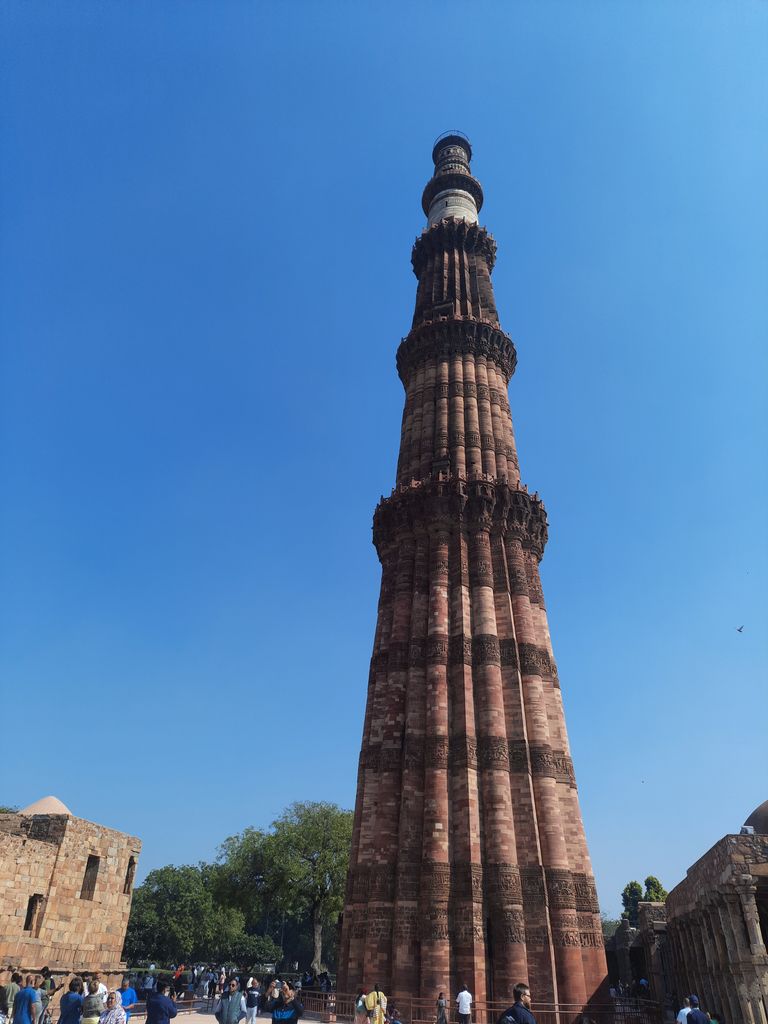 The tapering Qutb Minar rises through fluted reddish stages, bands and projecting galleries to a lighter upper section.