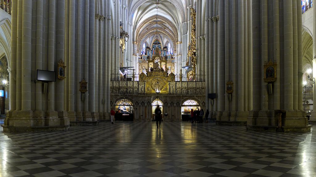 A decorated enclosure interrupts the central space between large nave piers, beyond a wide chequered floor and side passages.