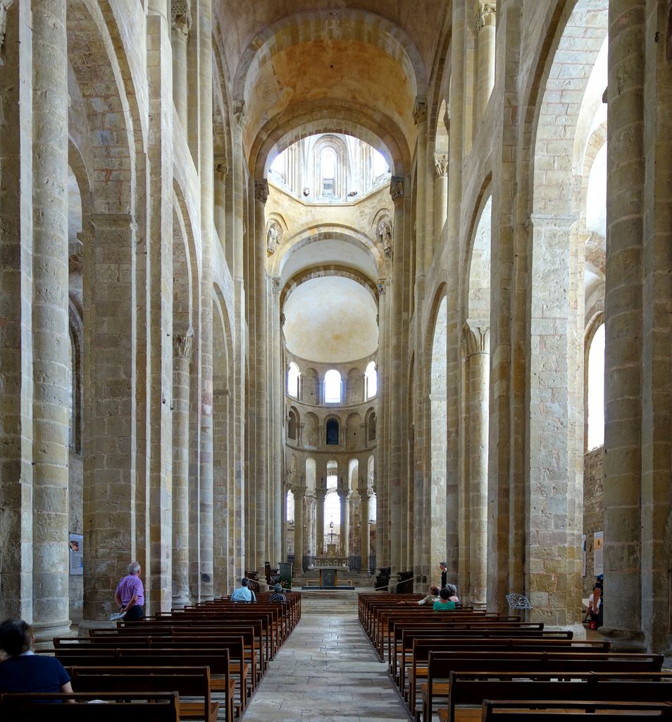 Tall stone piers flank benches and a central walkway leading beneath broad arches toward the crossing and a rounded apse.