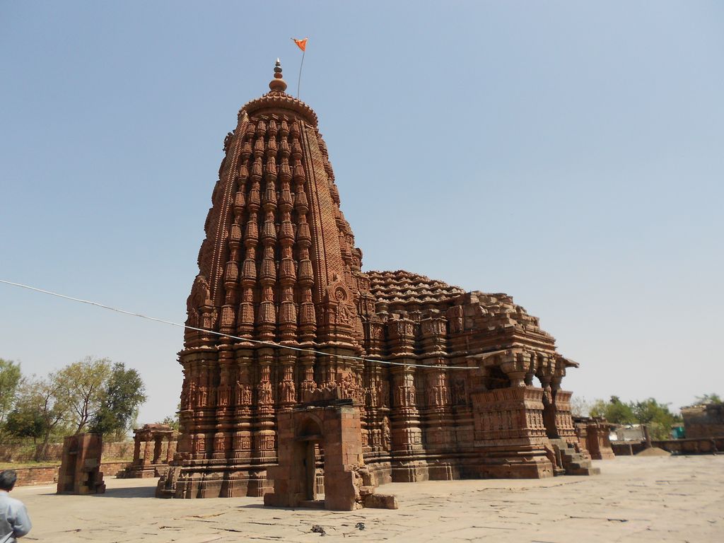 Rows of miniature spires and vertical stone bands cover a tall temple tower, with lower halls extending to the right.