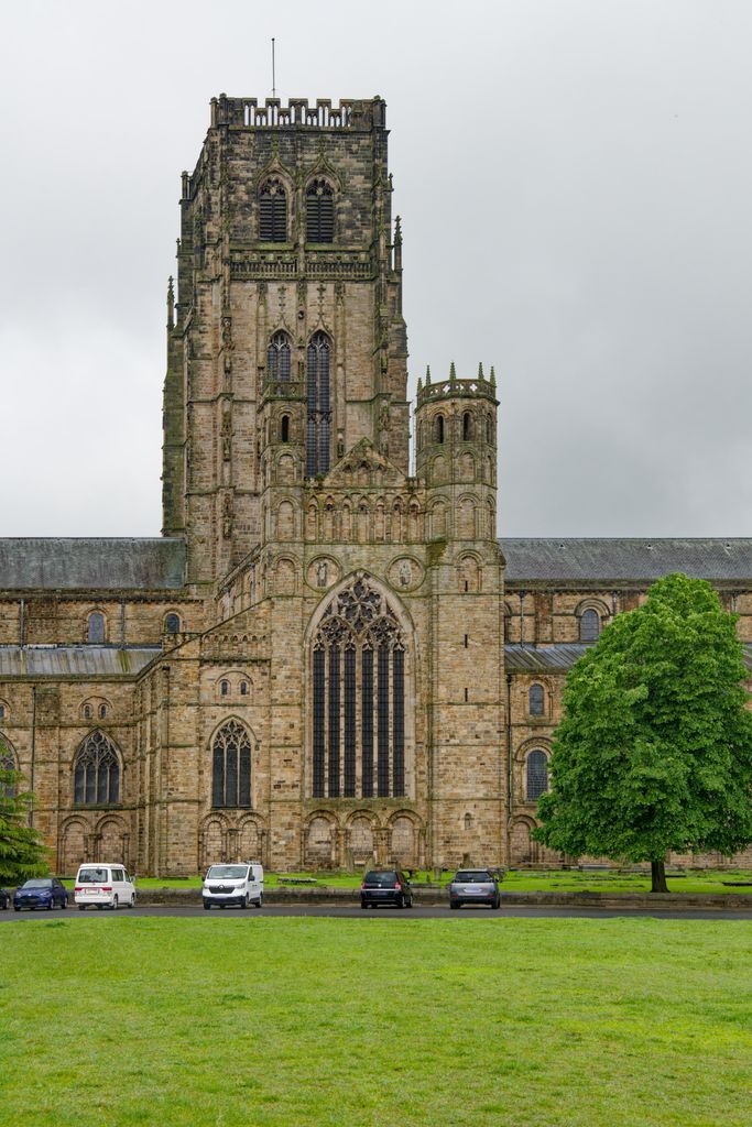 A gabled transept end with a large traceried window projects in front of a much taller square tower, with cathedral roofs continuing to either side.