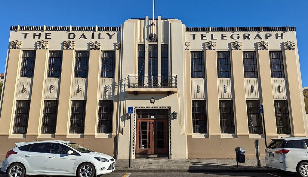 A symmetrical low-rise frontage uses tall window bays, stylised relief and a stepped central section beneath large lettering.