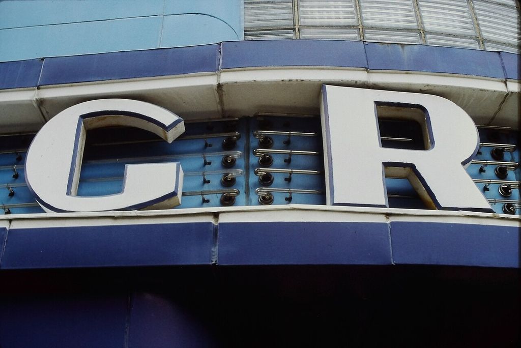 Exposed tubes sit within large projecting sign letters beneath a band of glass blocks.