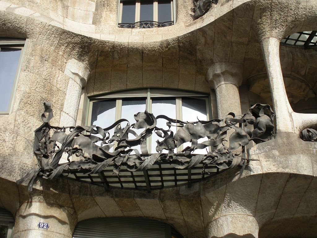 Twisting iron forms spread across a balcony set into an undulating stone façade.