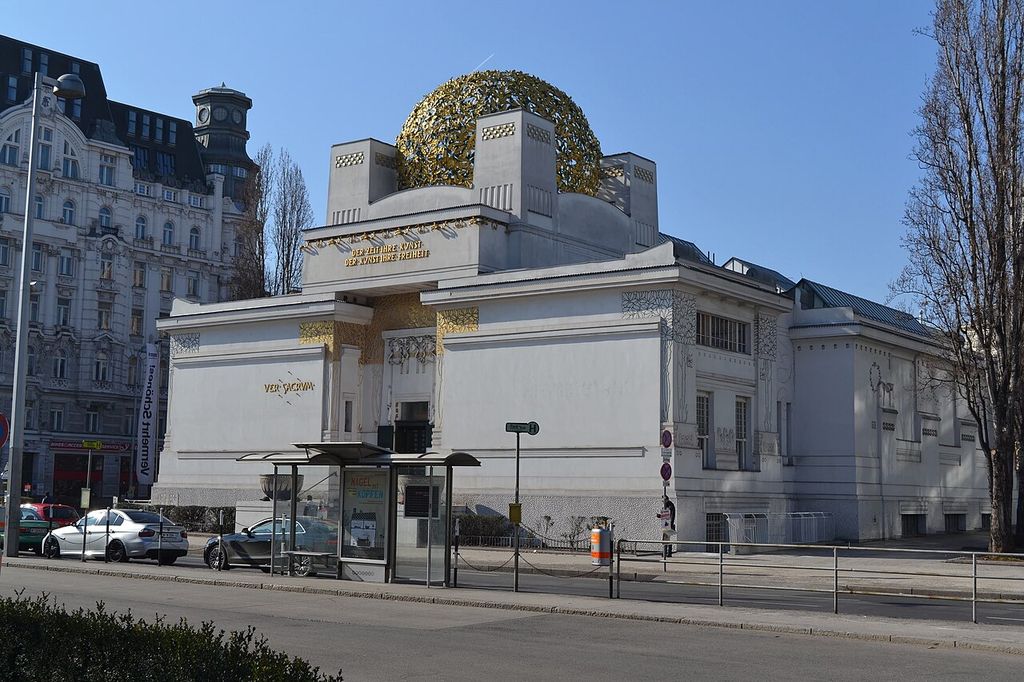 White cubic volumes rise beneath a golden openwork dome, with ornament concentrated around the entrance and roof.