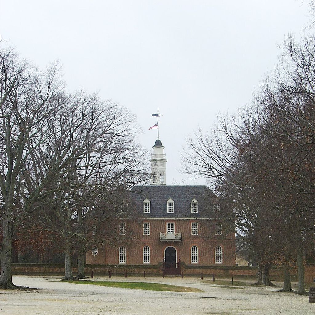 A brick elevation with an arched doorway, dormer windows and a cupola faces a gravel approach between winter trees.