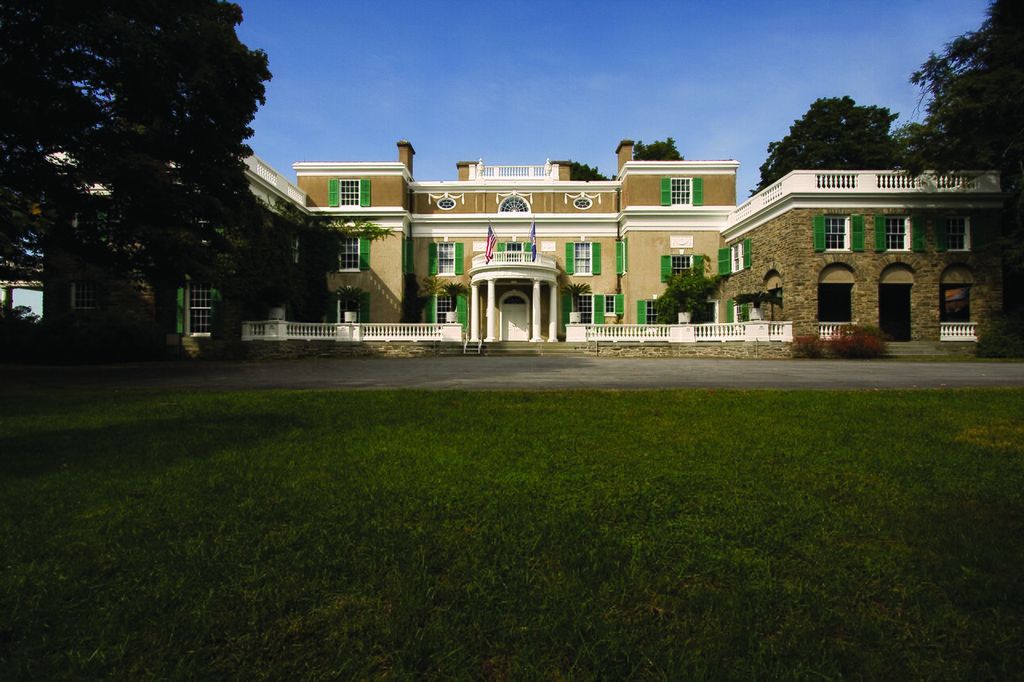 A semicircular columned entrance joins a central house to broad side wings with aligned windows and balustrades.