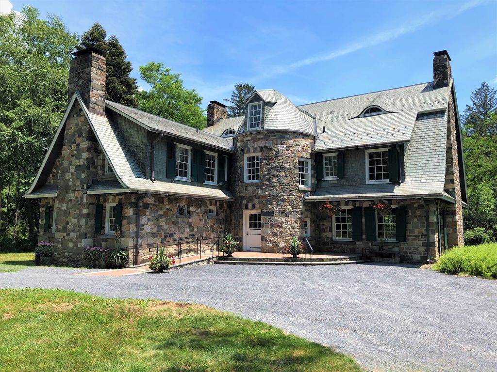 Two stone wings meet at a rounded entrance tower beneath steep, flaring roofs with dormers and tall chimneys.