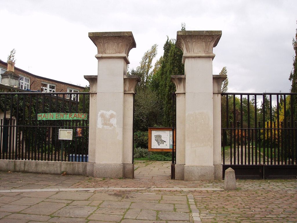 Tall pale gate piers with plant-patterned capitals flank an opening in iron railings.