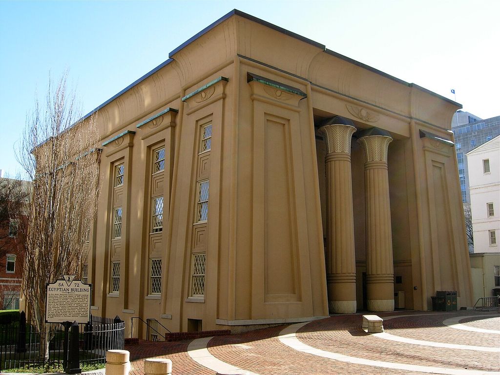 Sloping wall divisions, tall plant-patterned columns and a broad curved cornice mark a large institutional entrance.