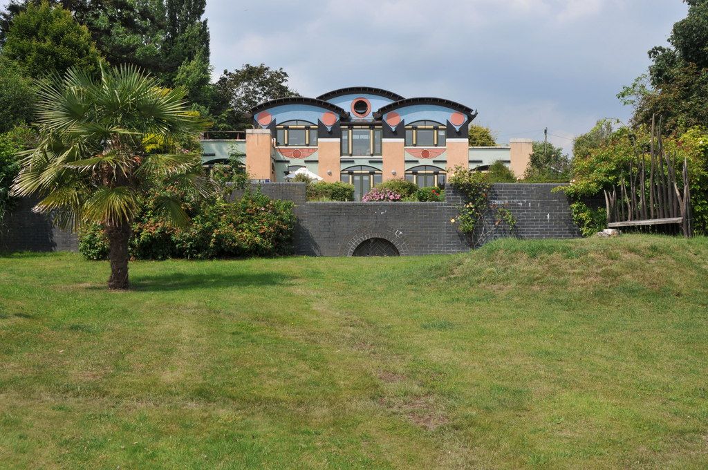A modern house with colourful geometric panels and curved roof profiles stands above a garden terrace.