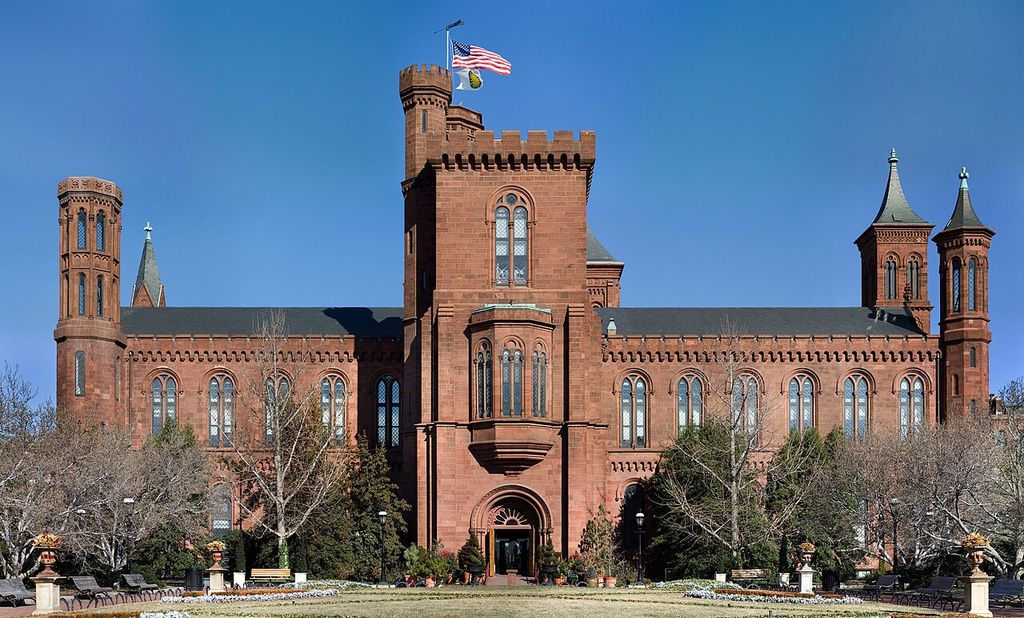 Red masonry walls with round-arched windows connect towers of different heights and roof shapes.