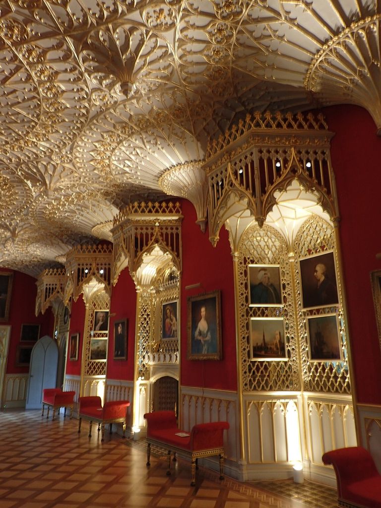 Gilded fan-like ceiling decoration and pointed canopies extend above red walls, pictures and chairs.