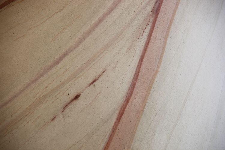 Reddish veins and fine speckles cross the pale curved surface of a plaster column.