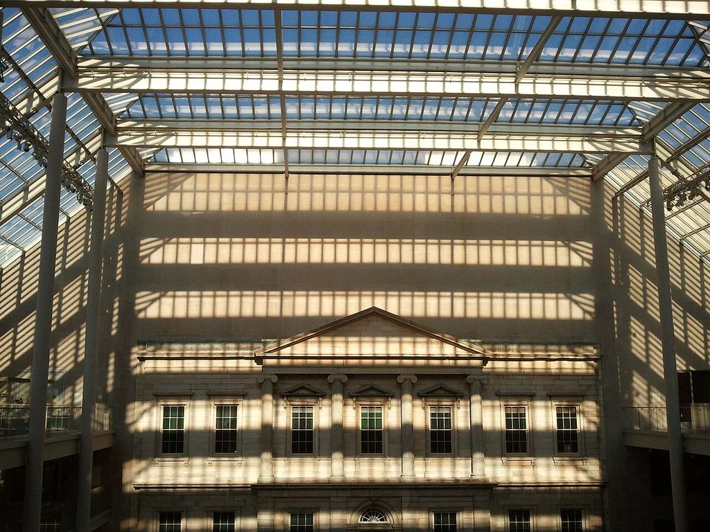 Ionic columns and a pediment stand beneath a modern glass roof inside a museum.