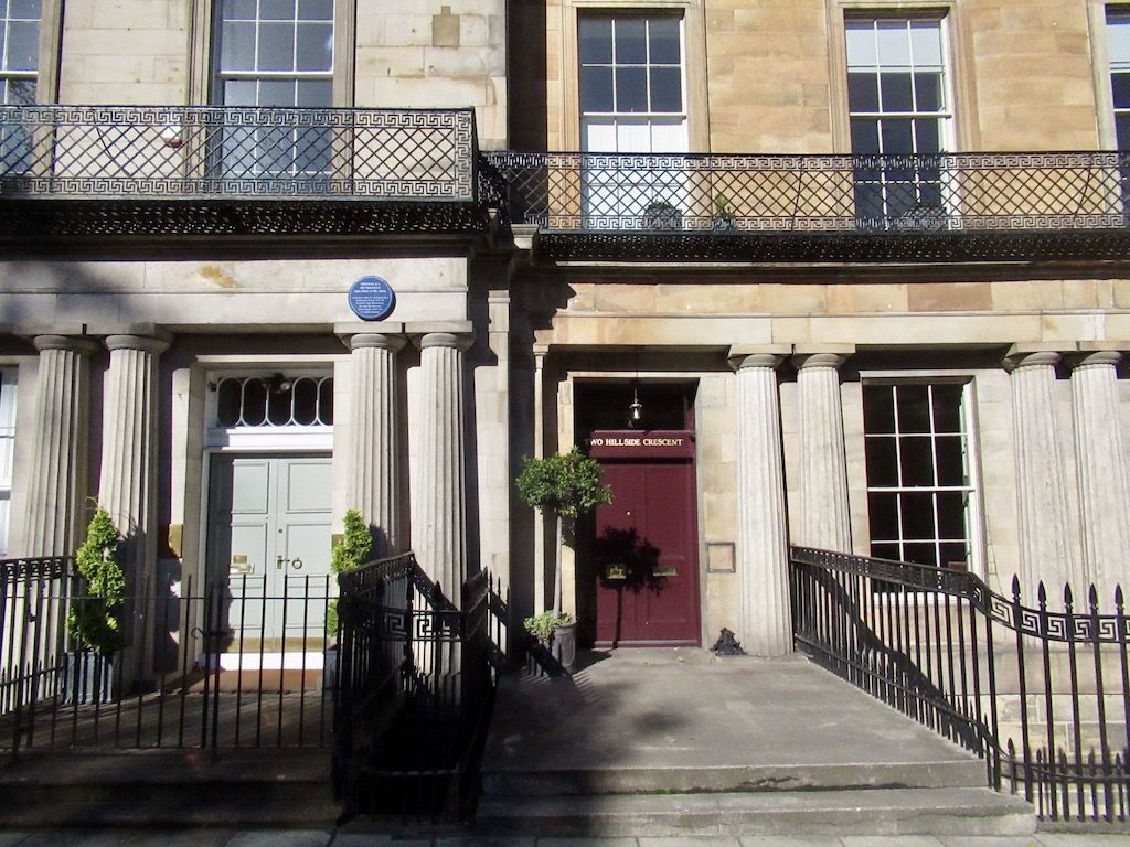Paired fluted columns frame townhouse doors below iron balconies edged with a Greek-key pattern.