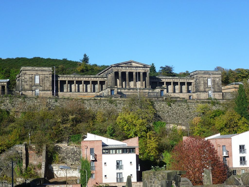A central temple-like portico and lower colonnades stand above a steep retaining wall and later buildings.