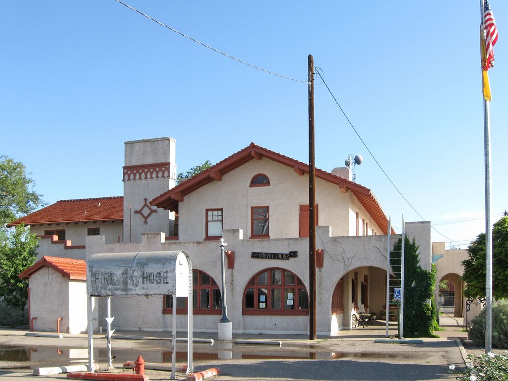 A two-storey stucco building with tiled roofs and a chimney stands behind a horseshoe-shaped entrance arcade and a Harvey House sign.