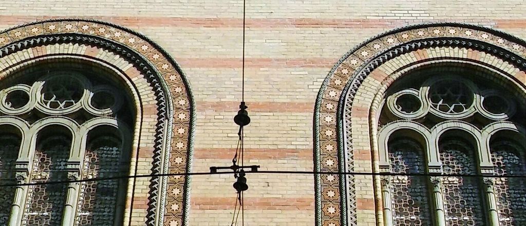 Two layered arched window heads with patterned star borders sit within horizontally banded brickwork.