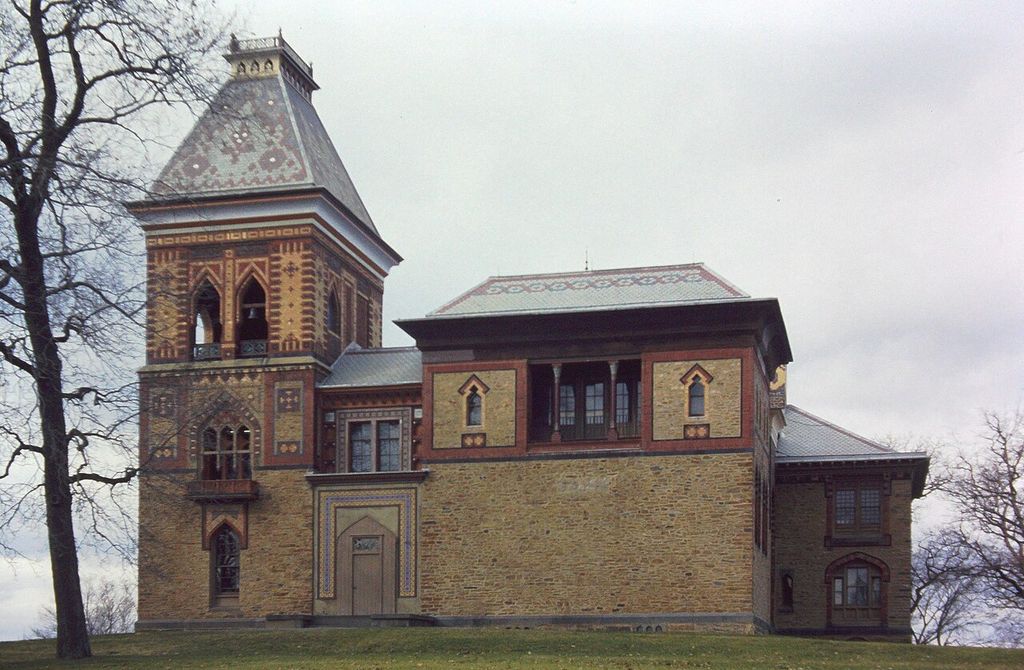 A tower and irregular house mass combine patterned roofs, coloured masonry and shaped openings.