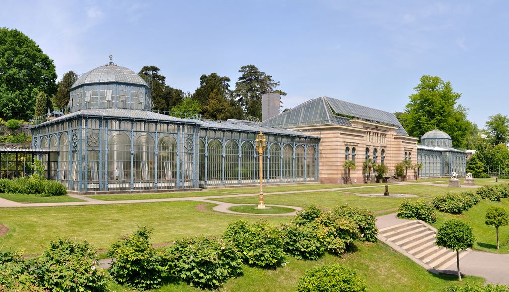A banded country house joins long glazed wings with circular iron patterns and domed ends beside formal lawns and paths.