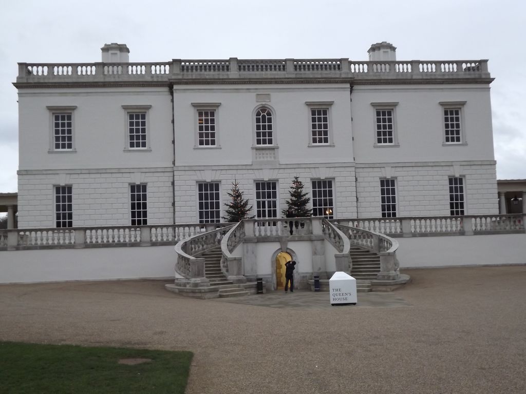 A symmetrical white house has a rusticated lower storey, balustraded roofline and paired curved stairs rising to a terrace.