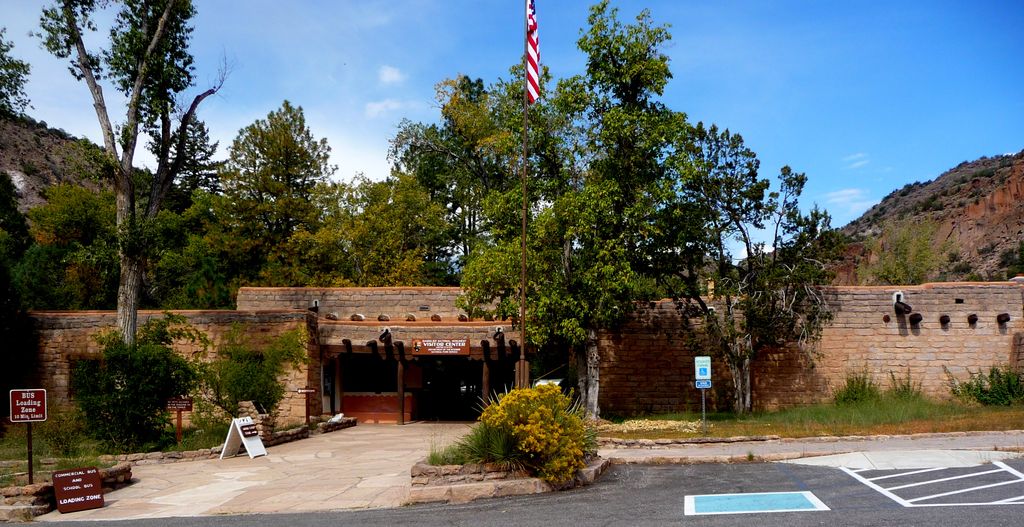 Low stone buildings and a timber entrance stand beside wooded canyon slopes and an accessible parking area.