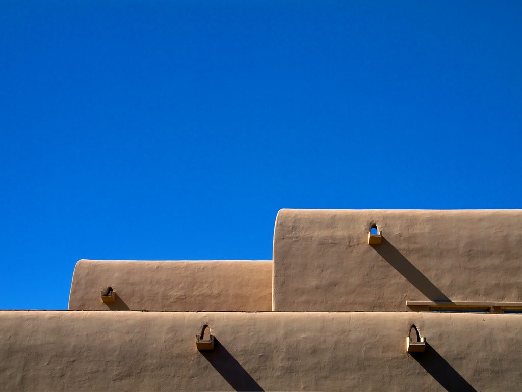 Three levels of rounded wall tops carry small projecting drainage spouts that cast long diagonal shadows.