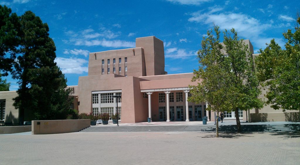 Tall stepped library volumes rise behind an entrance, broad paved approach and trees.
