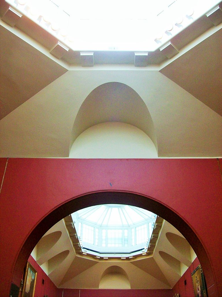 An arched opening connects gallery spaces beneath overhead glazing and curved ceiling surfaces.