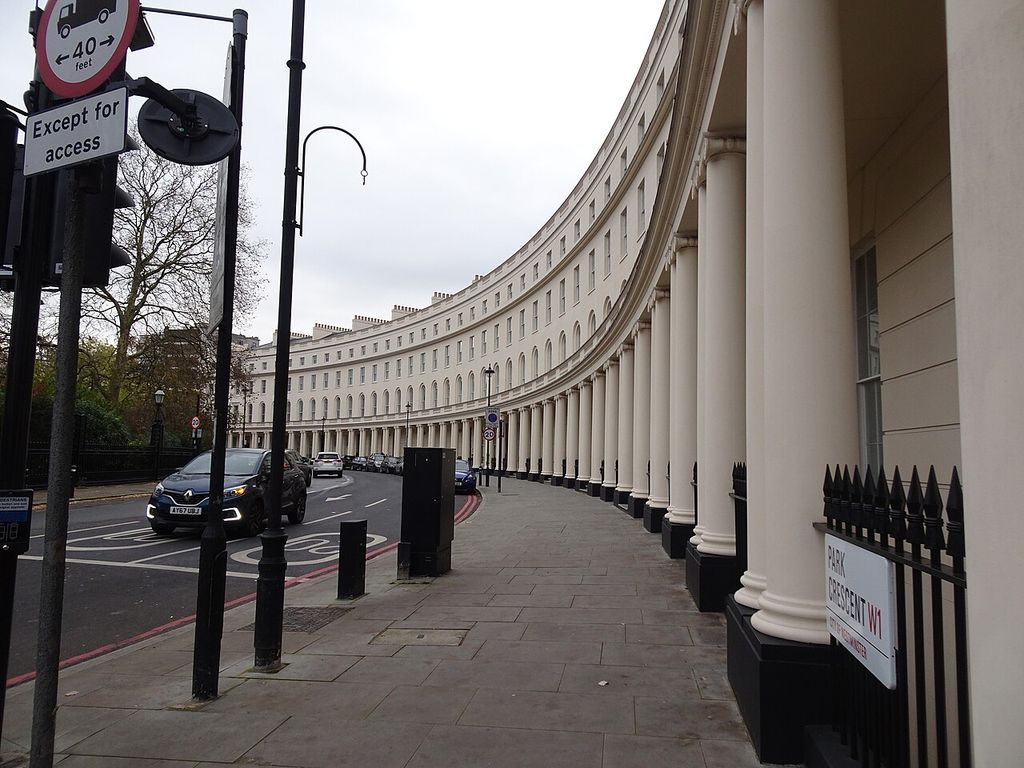 A pale colonnaded terrace curves along a street with repeated windows and a continuous cornice.