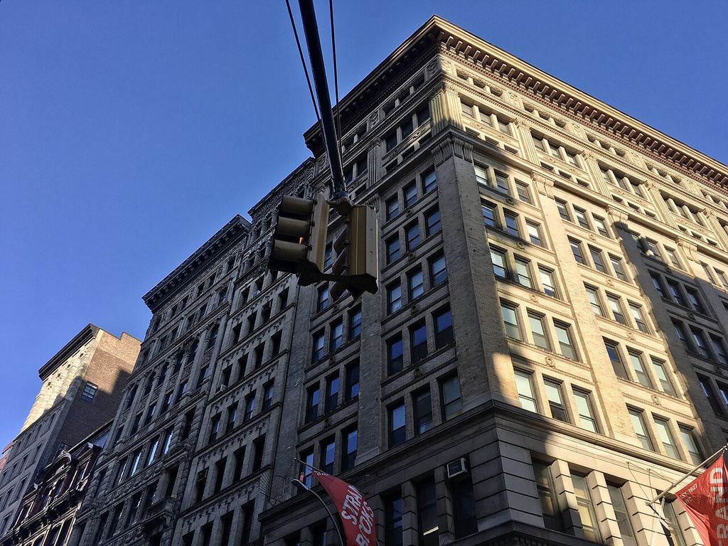 Regular rows of windows and upper pilasters rise to a deep cornice on a tall corner building.