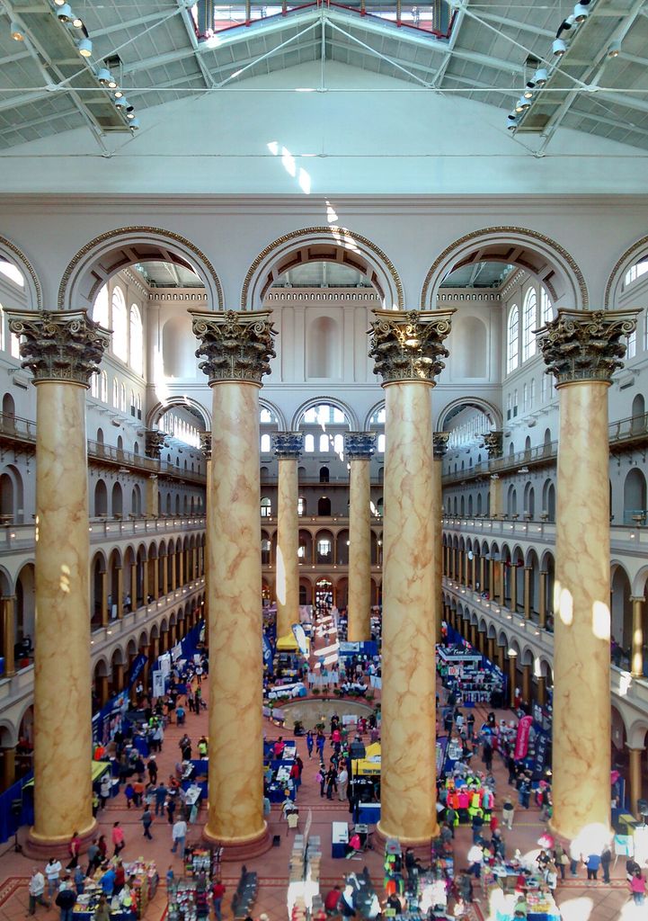 Colossal painted columns stand between tiers of arcades above a hall filled with visitors and temporary displays.