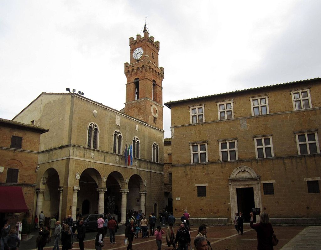 Arcaded town hall with a clock tower beside an ordered stone façade on Pienza’s Piazza Pio II.