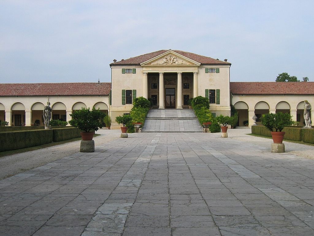 Temple-fronted villa approached by a broad ramp, with lower ranges of round arches extending to either side.