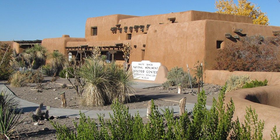 Rounded earth-coloured walls and projecting timber ends rise behind a desert plant garden.