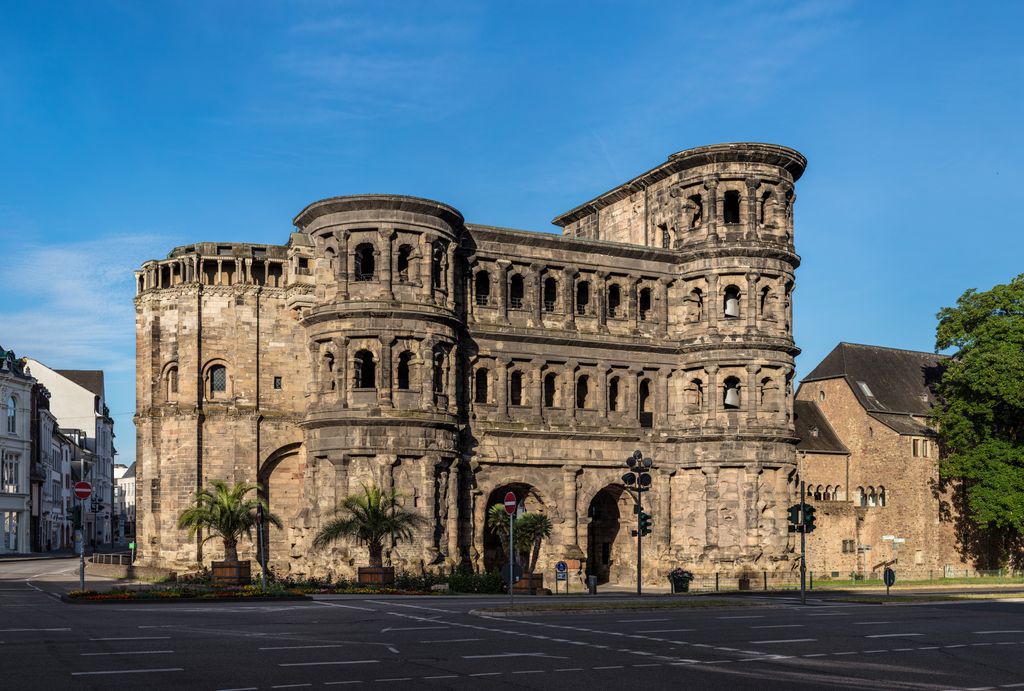 Two arched passages and rounded multi-storey towers of the Porta Nigra beside a modern street in Trier.
