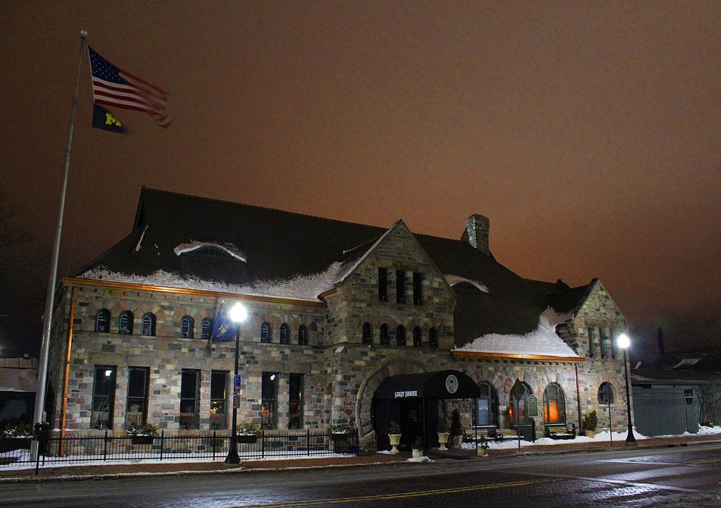 A stone station building has broad arches, grouped small windows and steep gables above a snowy pavement.