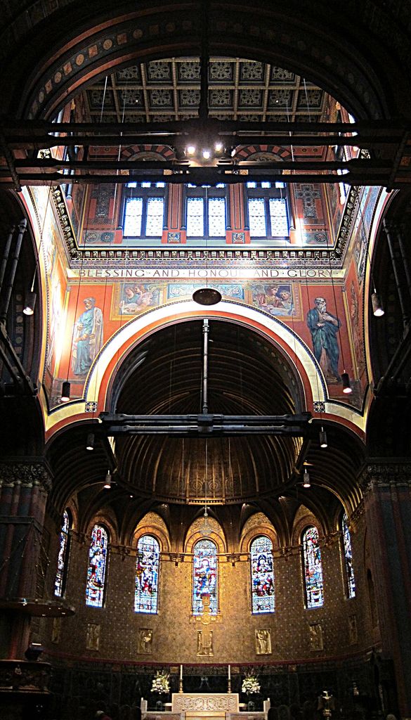 Painted figures and patterned bands surround large arches above a curved sanctuary wall and stained-glass windows.