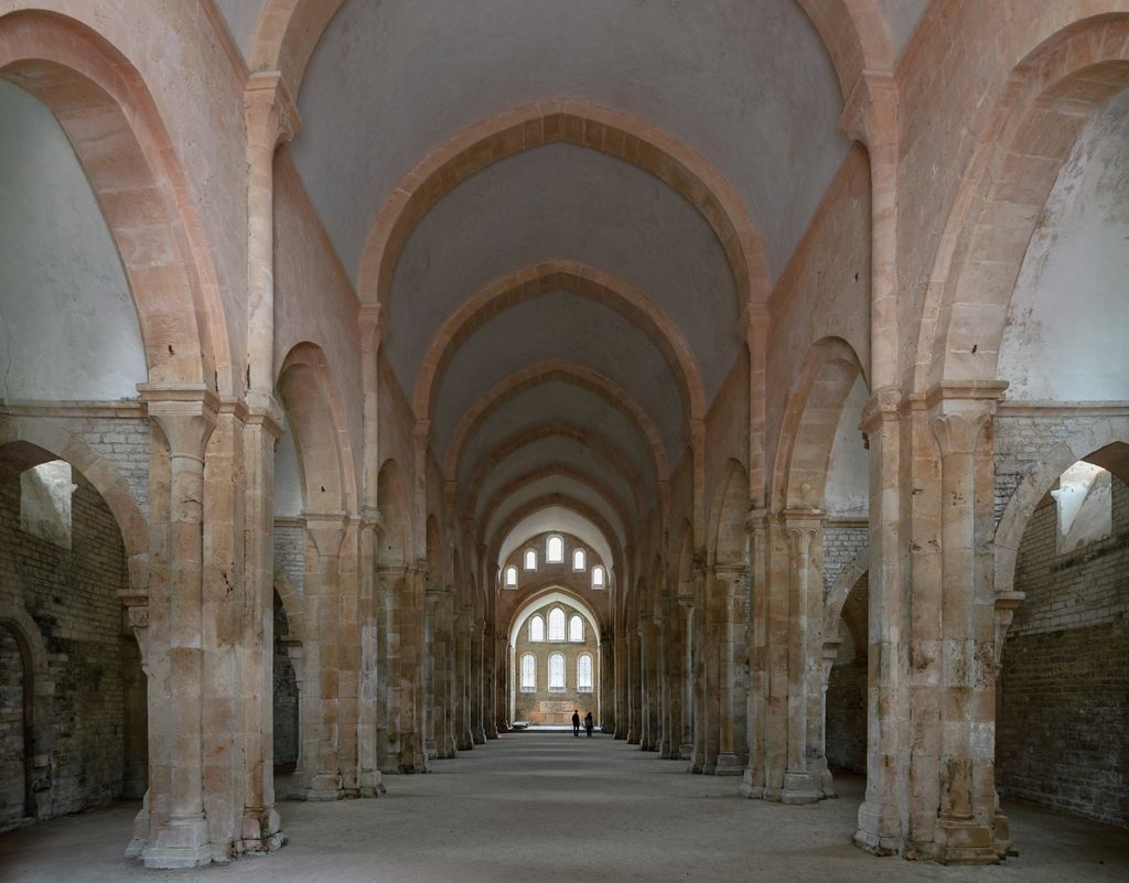 Repeated pointed stone arches and attached piers frame Fontenay’s long nave, with lower side arcades and bright windows ahead.