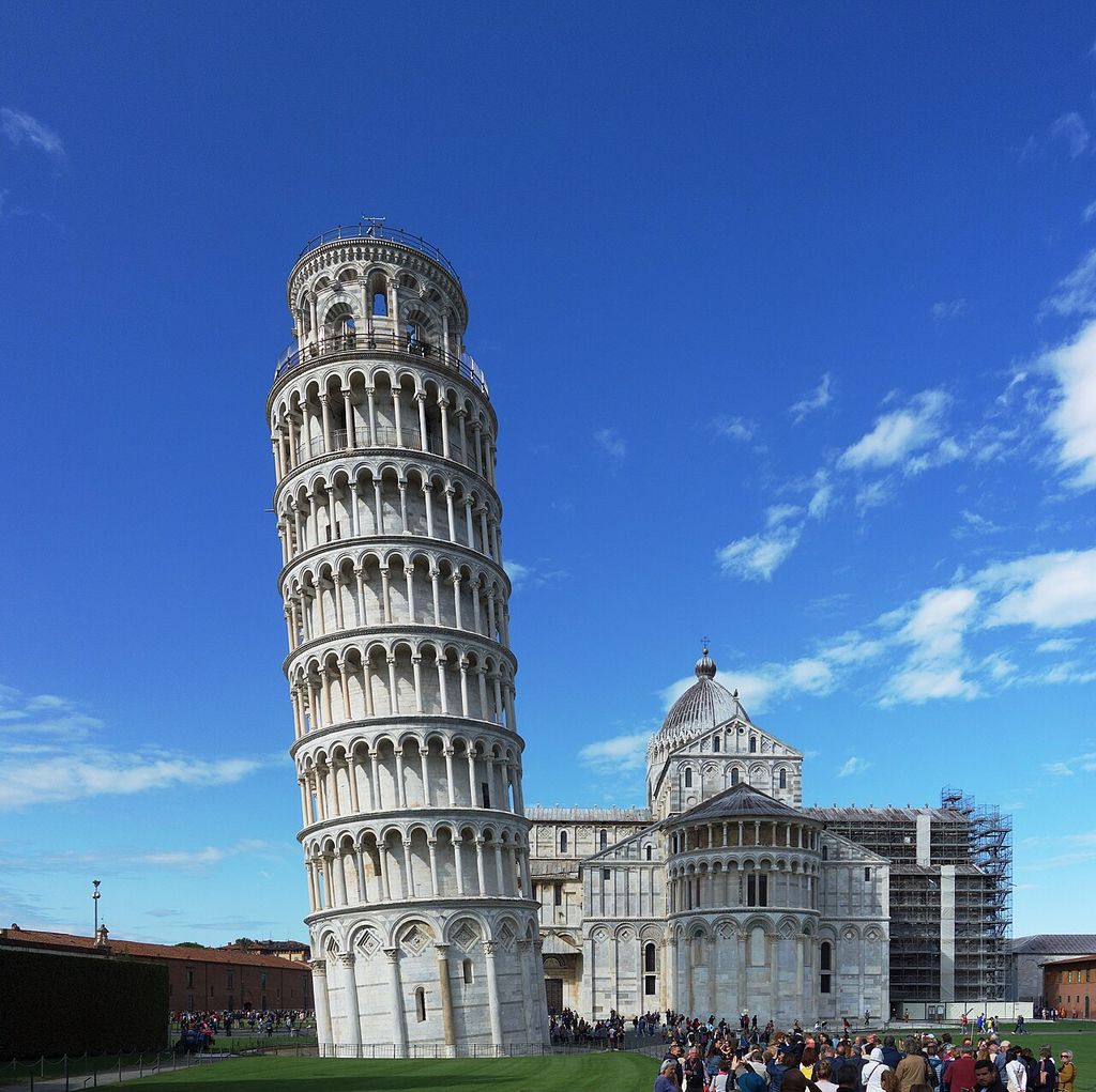 The Leaning Tower’s stacked marble arcades rise beside Pisa Cathedral’s apse and dome, with scaffolding on the right.