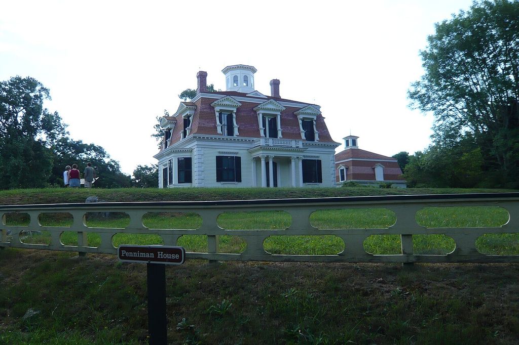 A house with pedimented dormers, a mansard and a cupola stands on raised ground beside a barn.