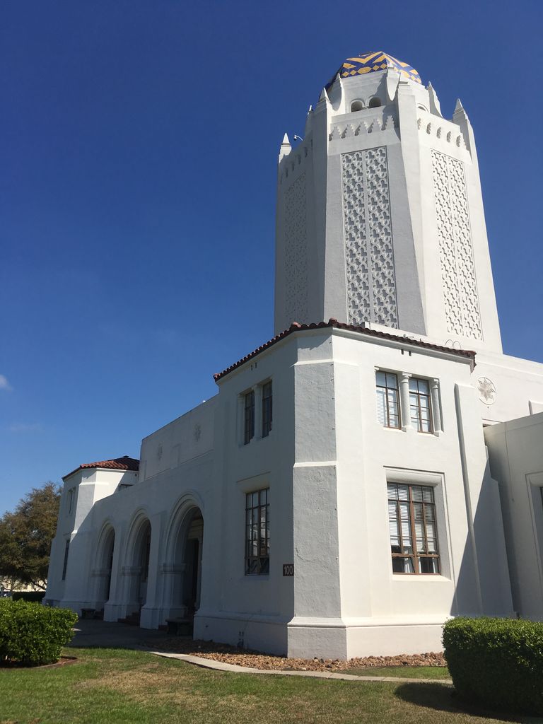 A white tower with patterned screens and a blue-and-yellow dome rises above an arched entrance and rectangular windows.
